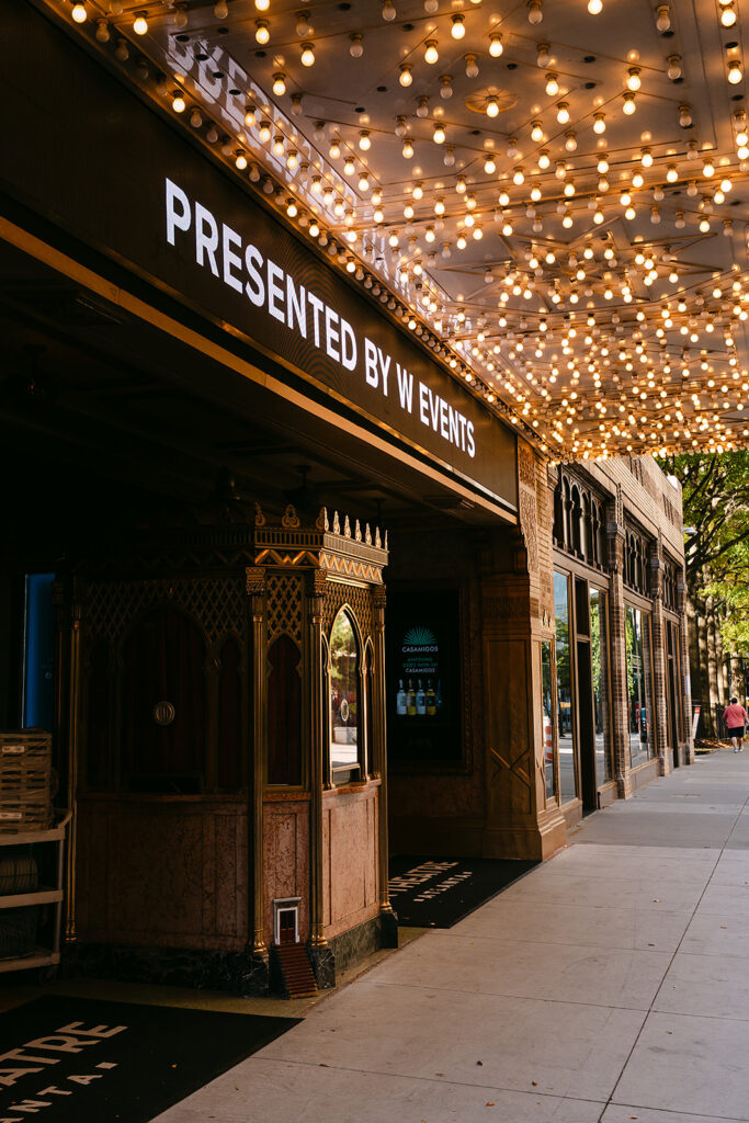 Exterior shot of the Fox Theatre in Atlanta featuring its glowing marquee filled with hundreds of warm bulbs. The sign reads “Presented by W Events,” casting light over the ornate ticket booth and historic architectural details along the sidewalk.