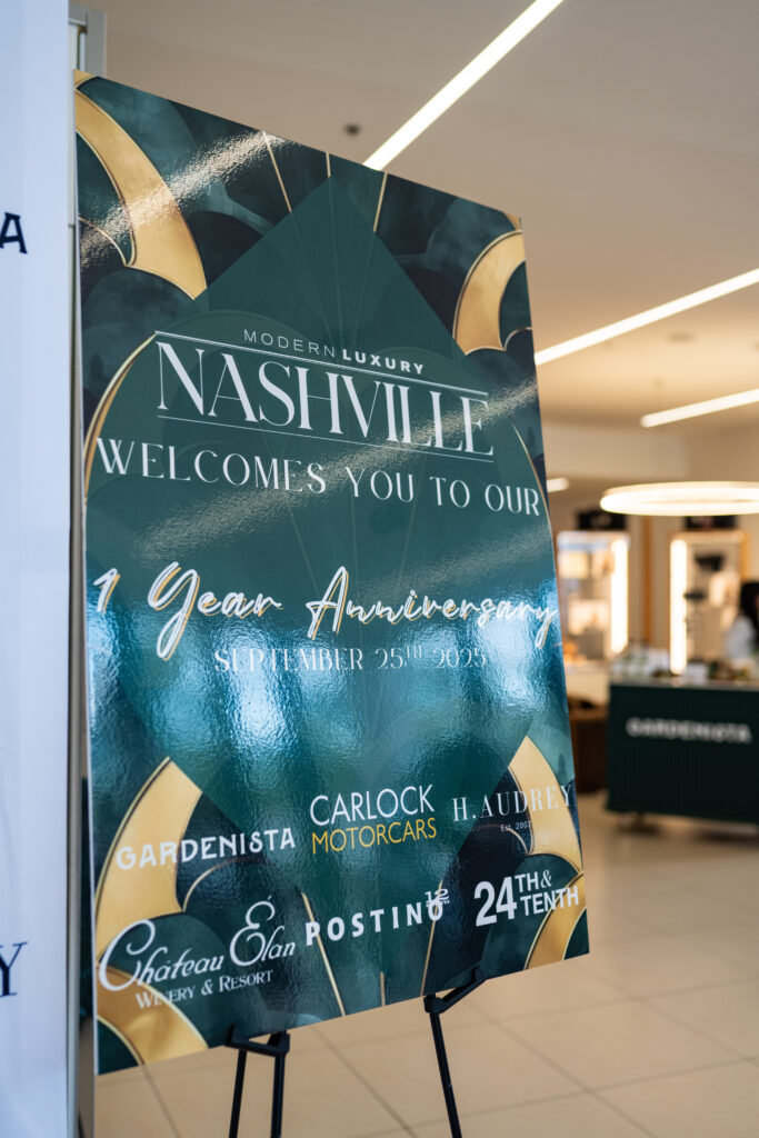 Modern Luxury Nashville one-year anniversary welcome sign in green and gold displayed at Carlock Motors in Nashville, featuring event sponsors and Art Deco–inspired design elements inside the transformed showroom venue.