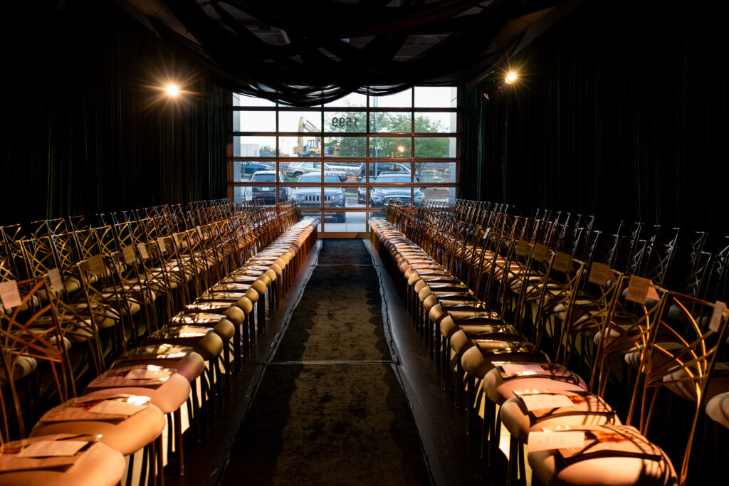 Runway-style seating with gold chairs and dramatic draping inside Carlock Motors during the Modern Luxury Nashville one-year anniversary fashion show event.