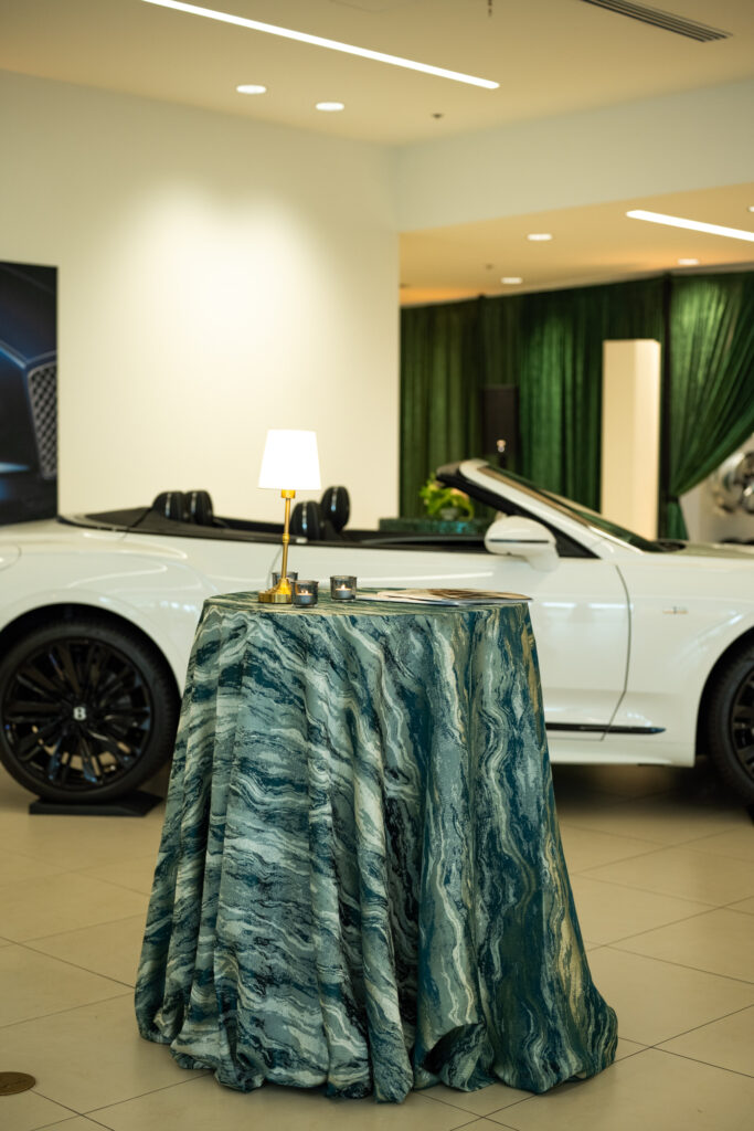 Green marbled cocktail table with gold lamp and candles set in front of a white luxury convertible inside Carlock Motors during the Modern Luxury Nashville one-year anniversary event.