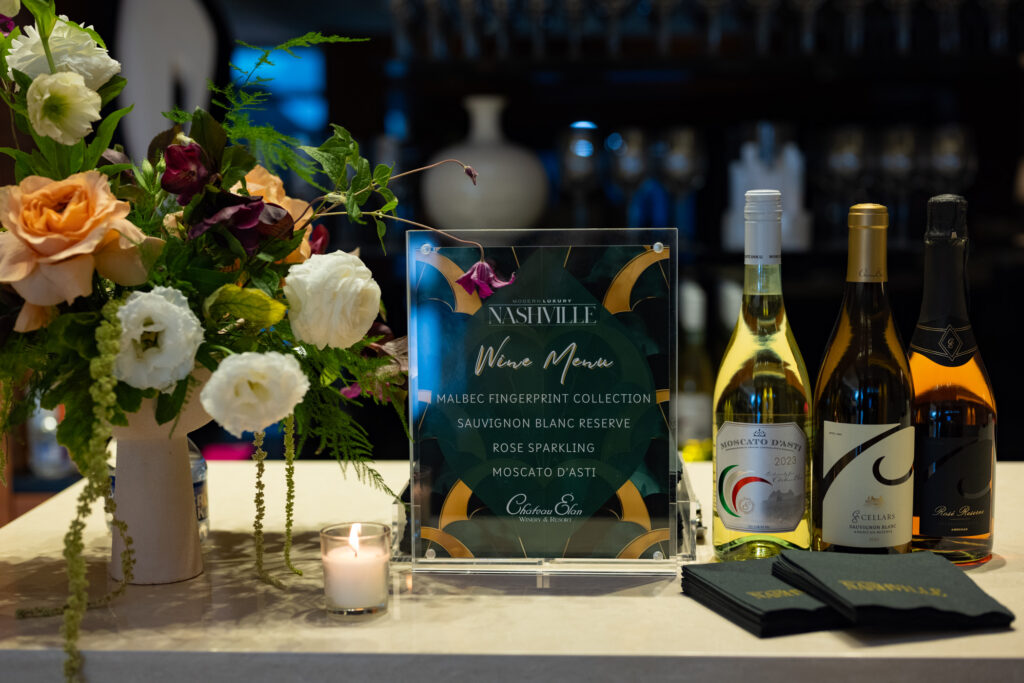 Chateau Élan wine display with floral arrangement, candle, and wine menu signage at the Modern Luxury Nashville one-year anniversary event at Carlock Motors.