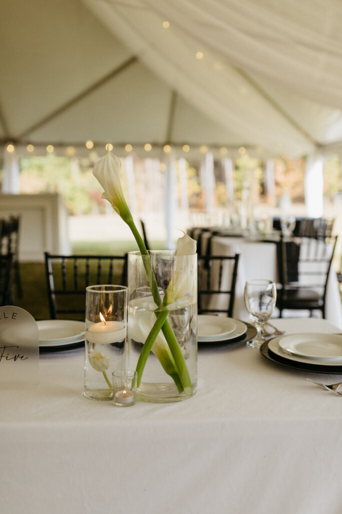 Minimalist calla lily centerpiece in clear glass vase with floating candles on a white linen table at tented wedding reception