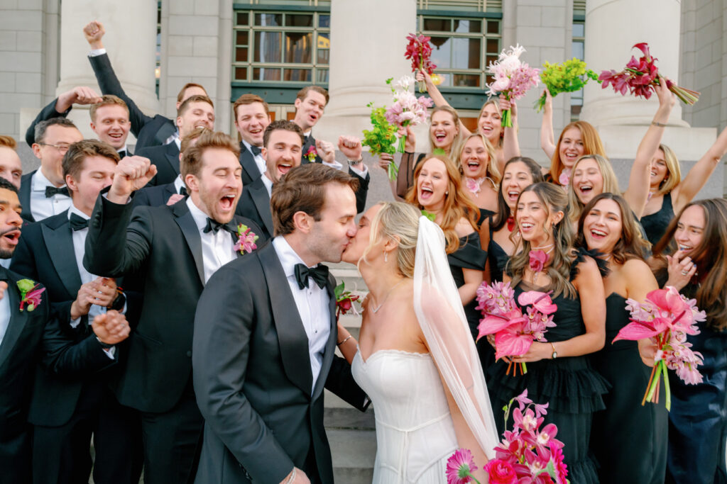 Bride and groom kissing with cheering bridal party holding pink and green bouquets at Nashville wedding