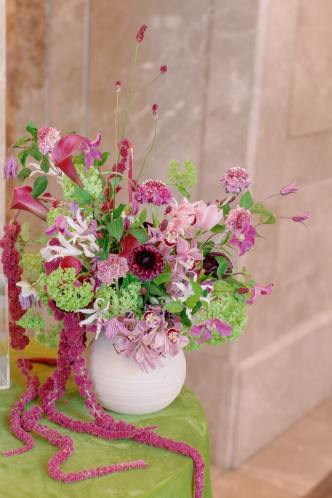 Wedding floral arrangement with pink, fuchsia, and green flowers in modern vase on chartreuse linen