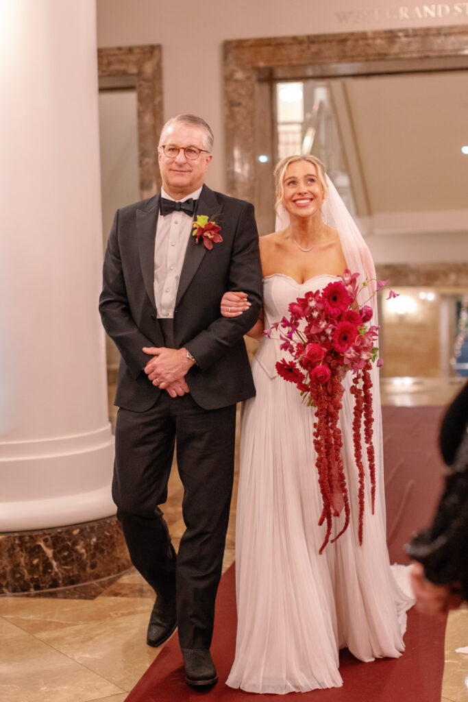 Bride walking down the aisle with her father holding fuchsia and burgundy bouquet at Nashville Symphony wedding