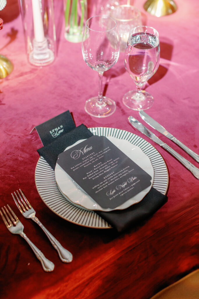 Wedding place setting with black menu card, layered plates, and burgundy linen at Nashville Symphony reception