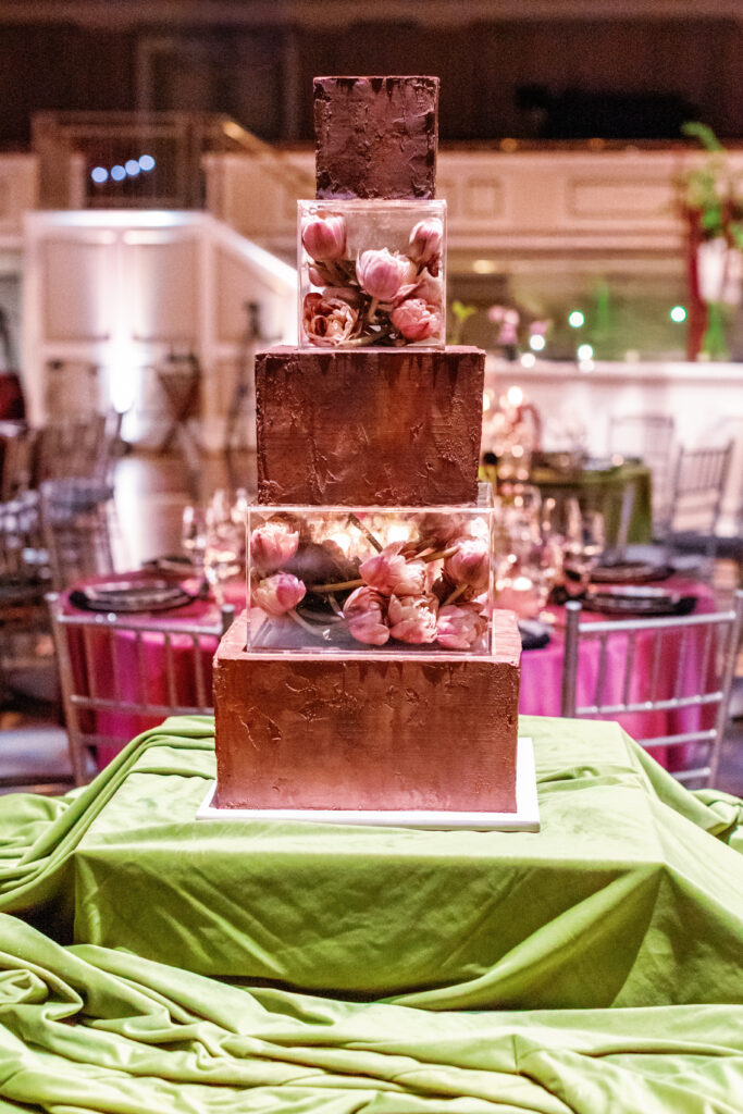 Modern wedding cake with textured tiers and clear layers filled with pink flowers on chartreuse linen table