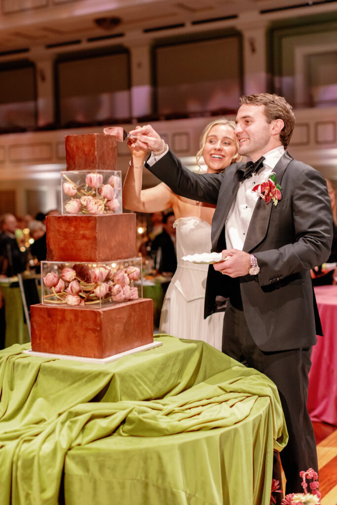 Bride and groom cutting modern wedding cake with floral acrylic layers at Nashville Symphony reception